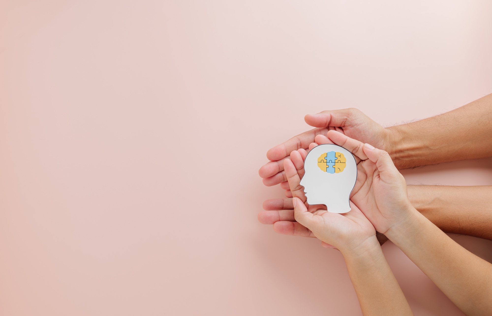 Hands of adult and child holding a brain jigsaw in a head paper cut highlight Down Syndrome