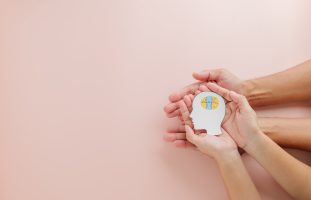 Hands of adult and child holding a brain jigsaw in a head paper cut highlight Down Syndrome